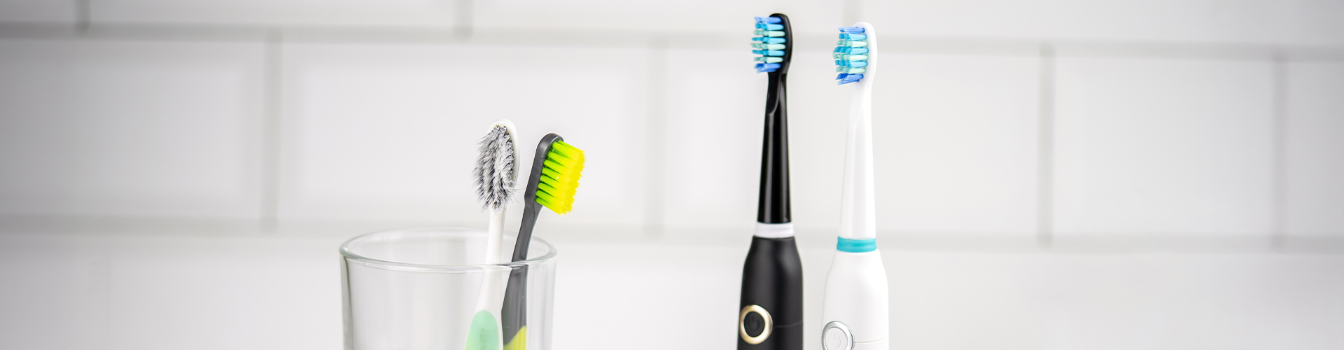 Electric and manual toothbrushes in front of white tile.